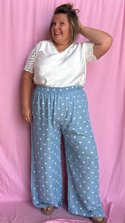 Avec sa coupe droite et jambes larges, ce pantalon fluide bleu ciel motifs coeur blanc est parfait pour bouger librement tout en étant stylée.