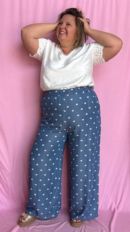 Avec sa coupe droite et jambes larges, ce pantalon fluide bleu jean motifs coeur blanc est parfait pour bouger librement tout en étant stylée.