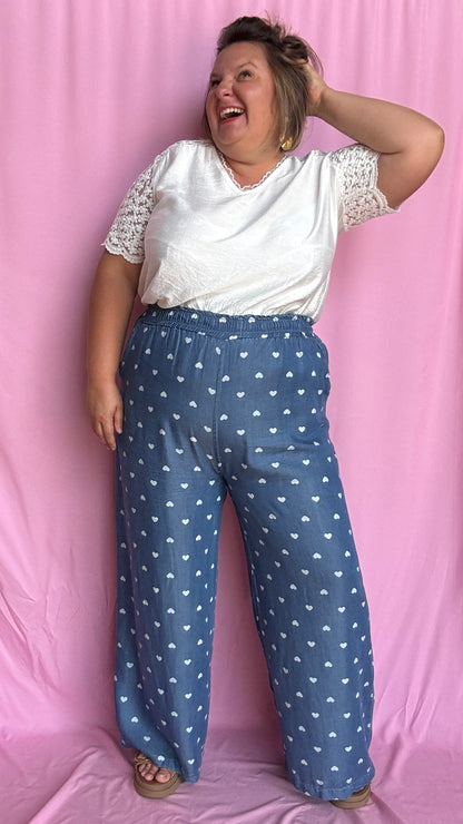 Avec sa coupe droite et jambes larges, ce pantalon fluide bleu jean motifs coeur blanc est parfait pour bouger librement tout en étant stylée.