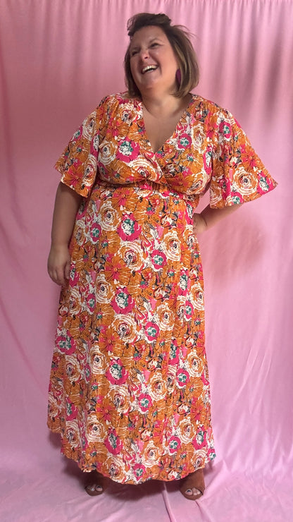 Un vent de fraîcheur et de féminité souffle sur ta garde-robe avec cette magnifique robe longue grande taille aux motifs fleuris dans des tons orange et rose 🌷