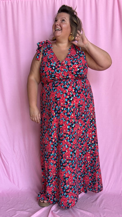 Une robe longue grande taille ultra féminine et pleine d'élégance, avec ses magnifiques motifs fleuris dans les tons rouge, bleu et doré et son dos nu.