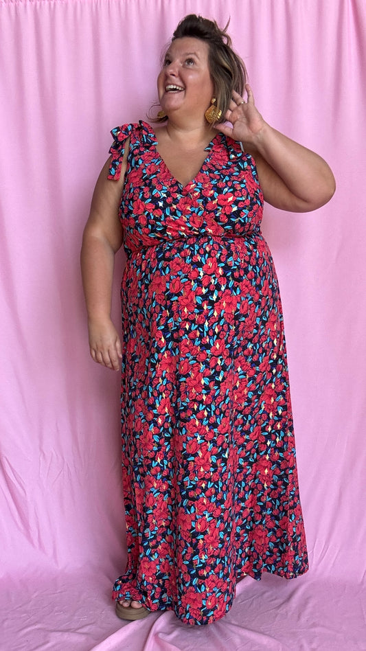 Une robe longue grande taille ultra féminine et pleine d'élégance, avec ses magnifiques motifs fleuris dans les tons rouge, bleu et doré et son dos nu.