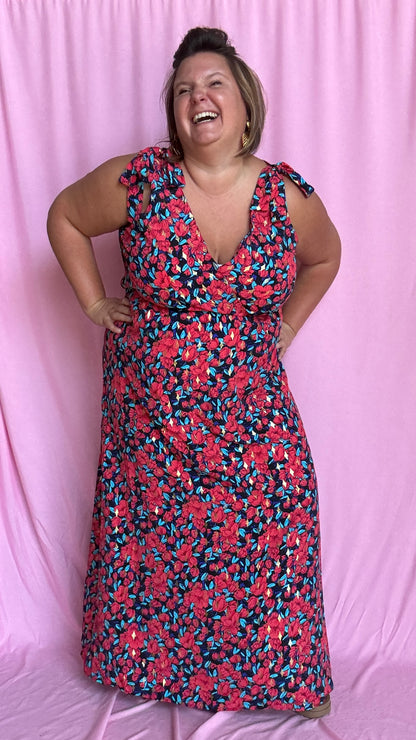 Une robe longue grande taille ultra féminine et pleine d'élégance, avec ses magnifiques motifs fleuris dans les tons rouge, bleu et doré et son dos nu.